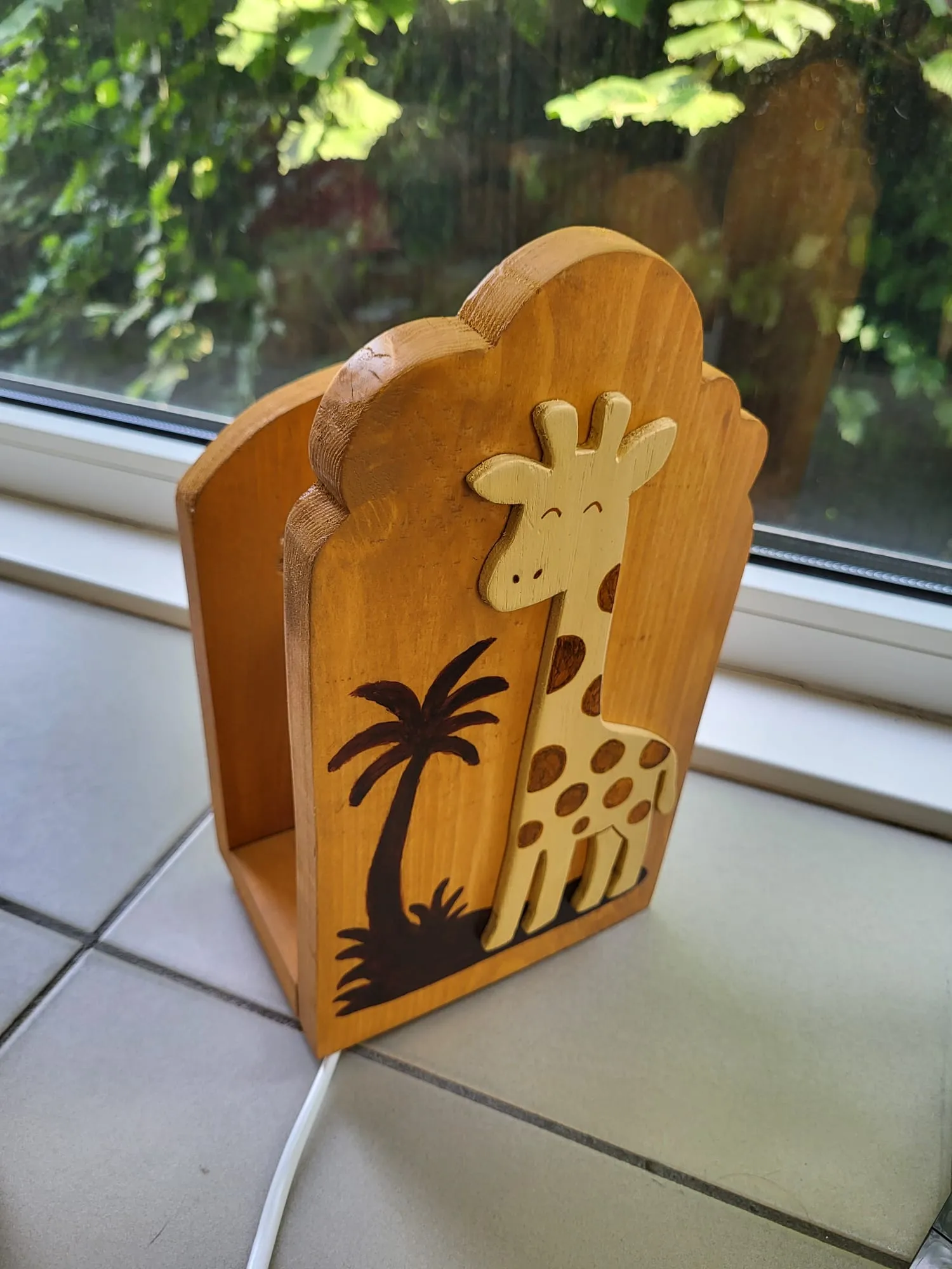 Houten figuur met een giraf en palmboom, voor het raam